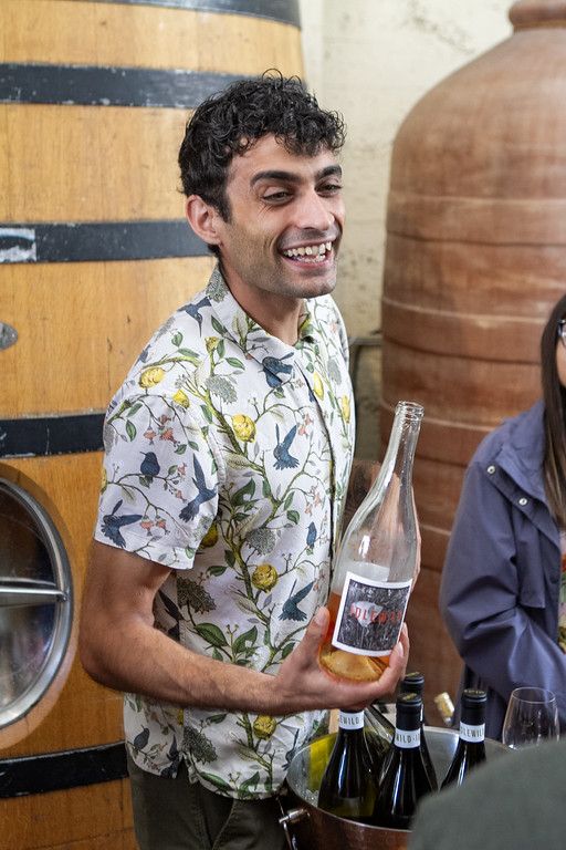 A winemaker holding a bottle by the barrels